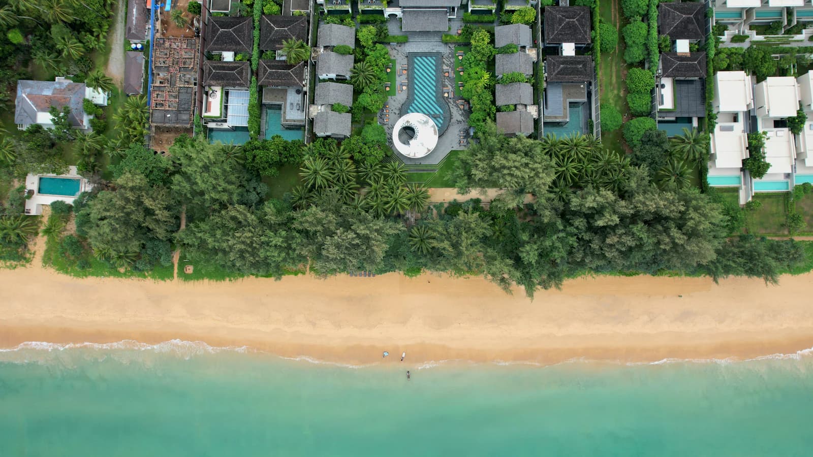 Aerial view of luxury villas, pools, palms, and a tropical beach.